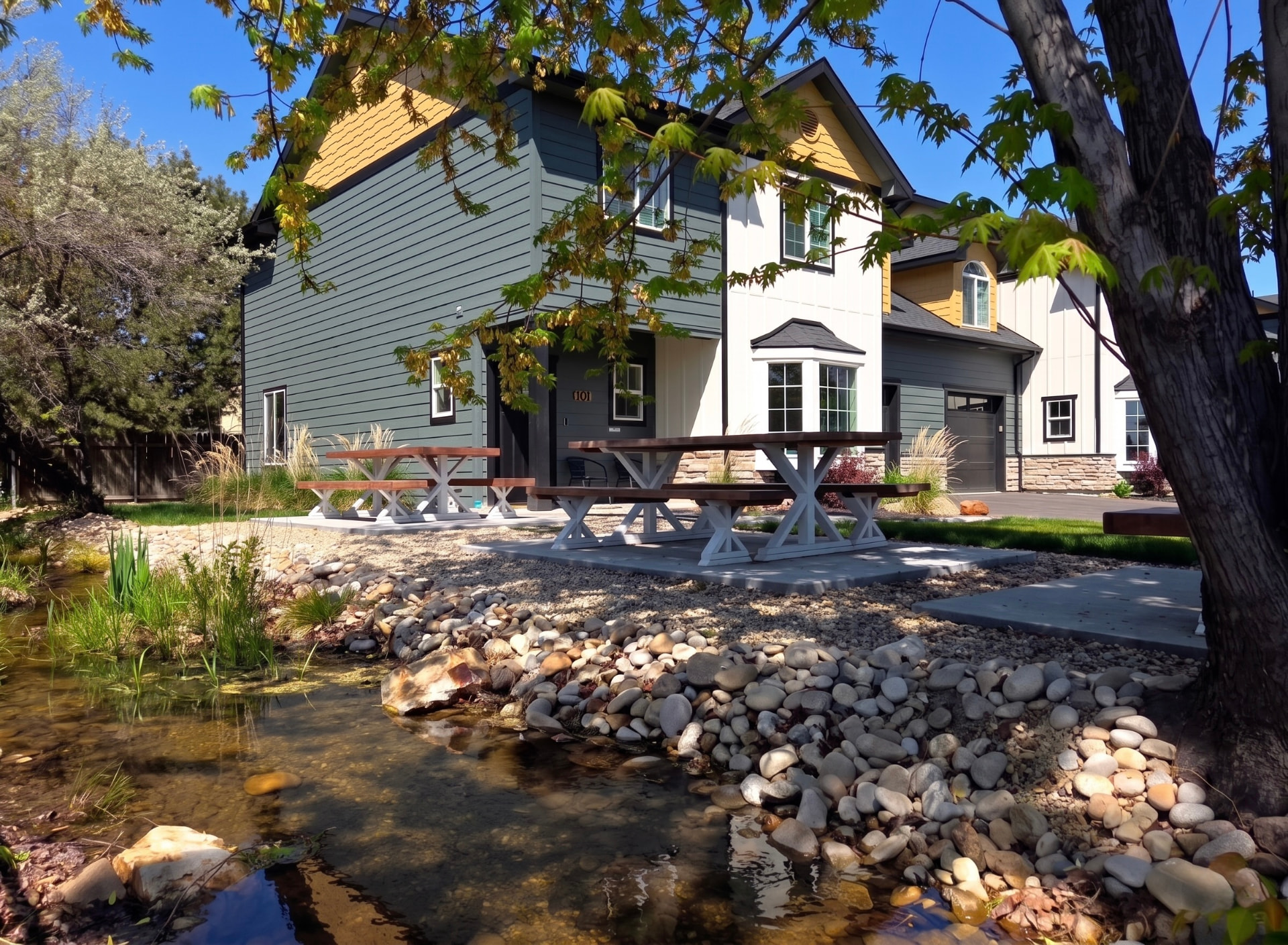Rising Sun Boise two-story home with slate-blue siding, shaded picnic tables, and a creekside patio